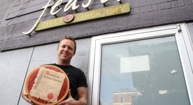 Co-owner Eric Gertner hoists a fragrant wheel o%2526#039; cheese outside the store.