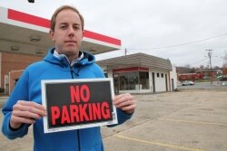 Nicholas Rigterink, standing on the sidewalk in front of the old Exxon, holds the type of sign he says might help prevent parking at the empty lot.