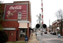 An old Coca-Cola sign adorns the side of a building by the train tracks.